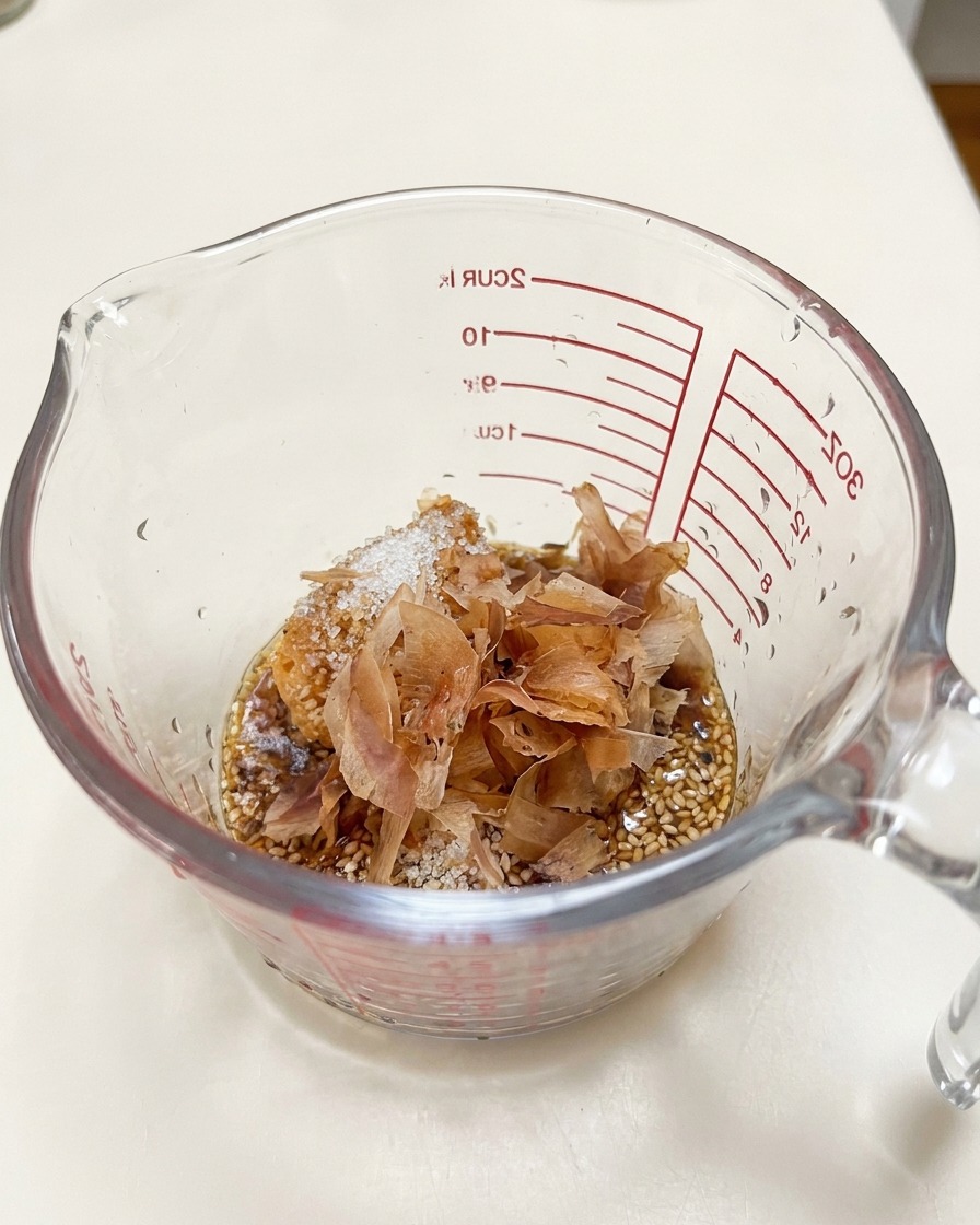 Bonito flakes layered on top of miso paste and sesame seeds inside a glass measuring cup.