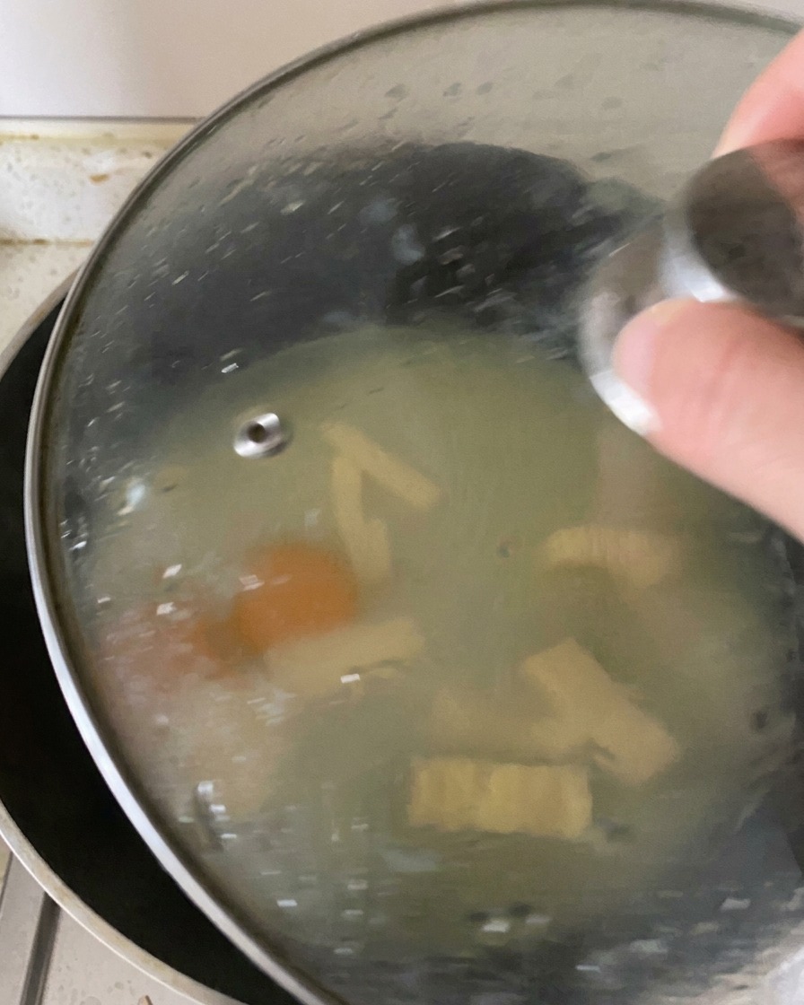 A glass lid placed over a frying pan, trapping steam inside to cook the eggs and melt the cheese.