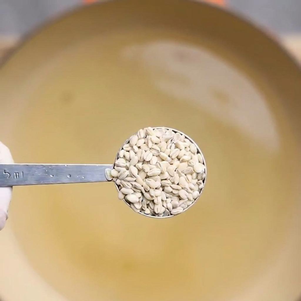 A measuring spoon lifting cooked barley out of a pot of boiling water.