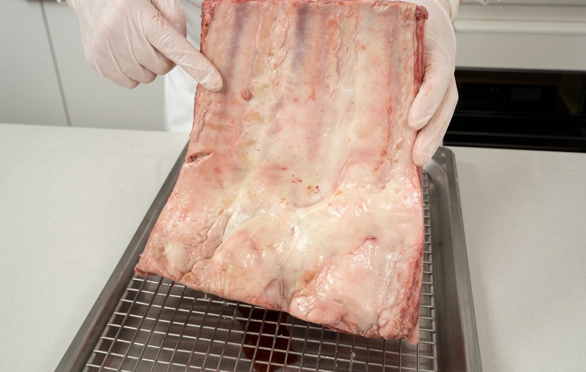 A chef holding up a raw rack of beef short ribs, showcasing the white fat marbling.