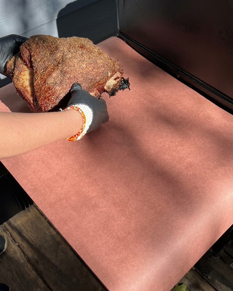 Gloved hands holding a large rack of smoked beef ribs with a dark spice crust, placing it down onto a sheet of pink butcher paper.