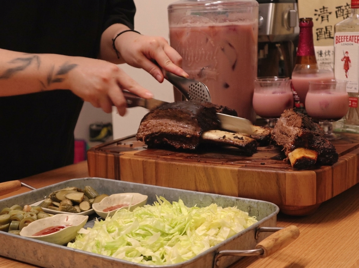 A platter featuring sliced roasted beef ribs with sides of lettuce, pickles, and bowls of red sauce.