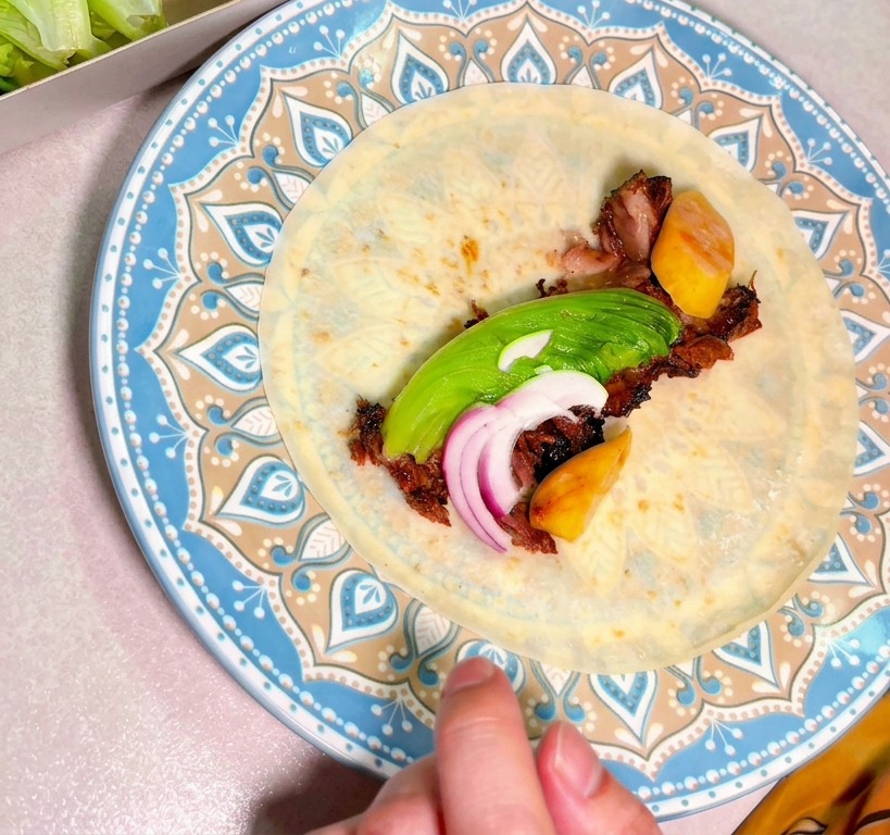 Chopped smoked beef topped with sliced avocado and red onions resting in the center of a tortilla on a decorative plate.