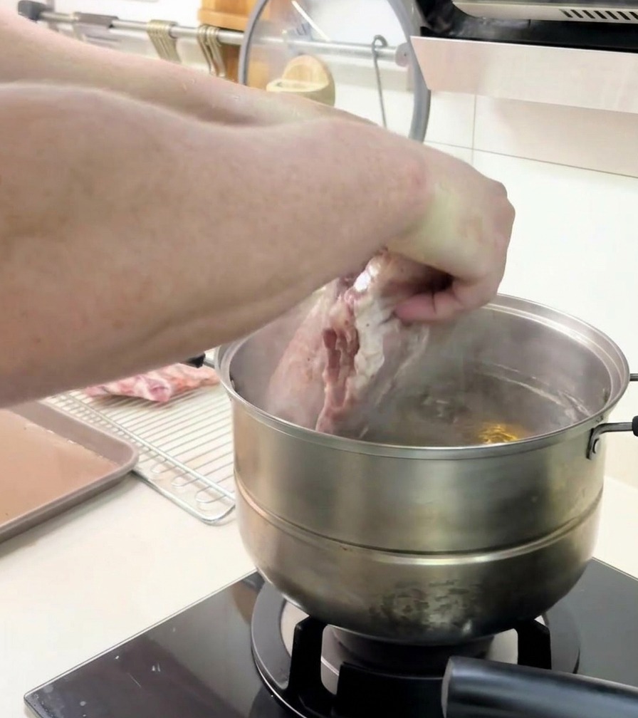 A person using both hands to carefully submerge a large rack of ribs into a steaming pot of water.