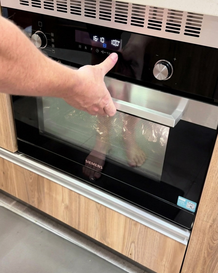 A hand pressing a button on a modern digital oven panel with the temperature set to 100 degrees.