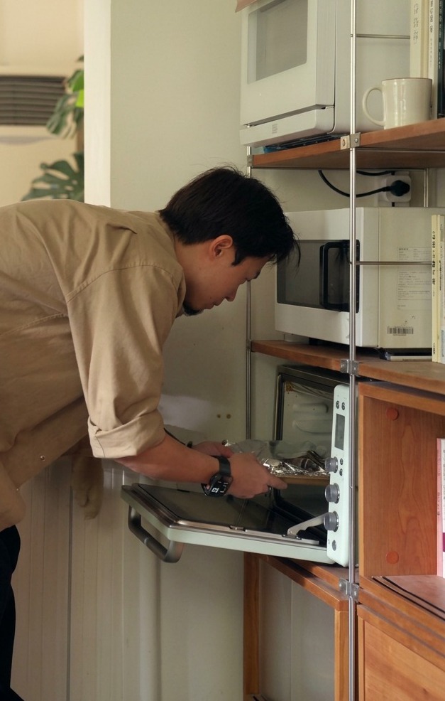 A tray of pork ribs wrapped securely in aluminum foil being placed into the rack of a preheated oven.