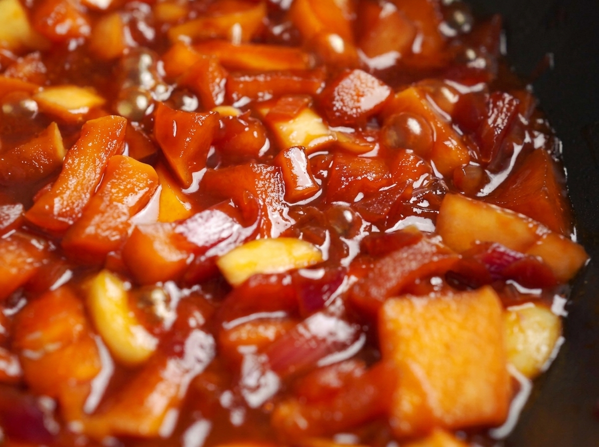 Diced apples and onions simmering in a rich, red sauce in a cooking pan.
