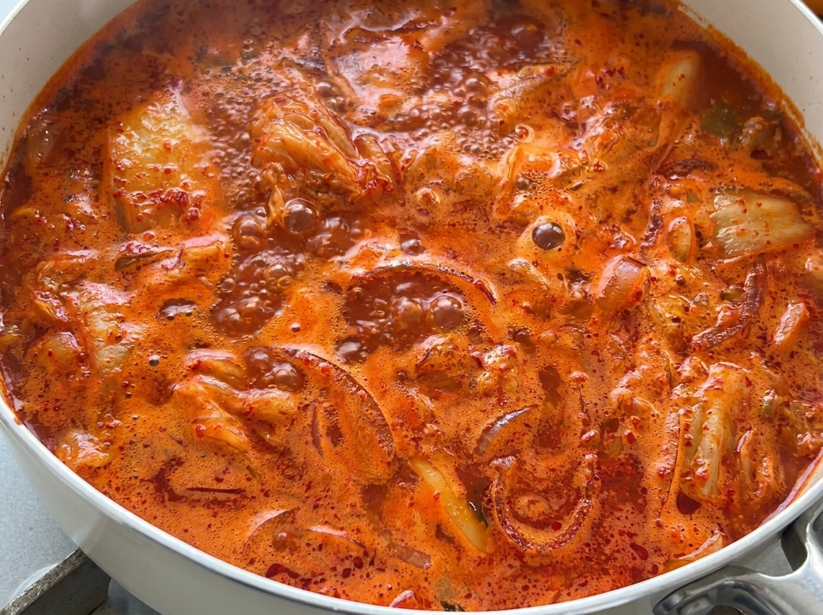 A close-up view of bright red kimchi soup boiling vigorously in a pan.