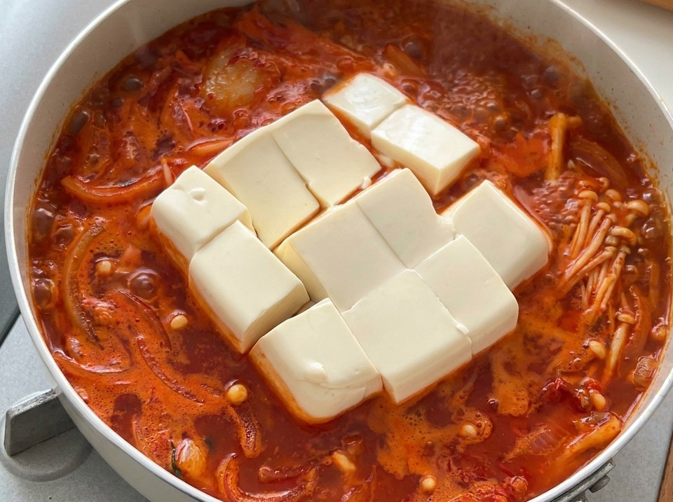Large cubes of soft white tofu sitting in a hot, bubbling Korean kimchi stew.