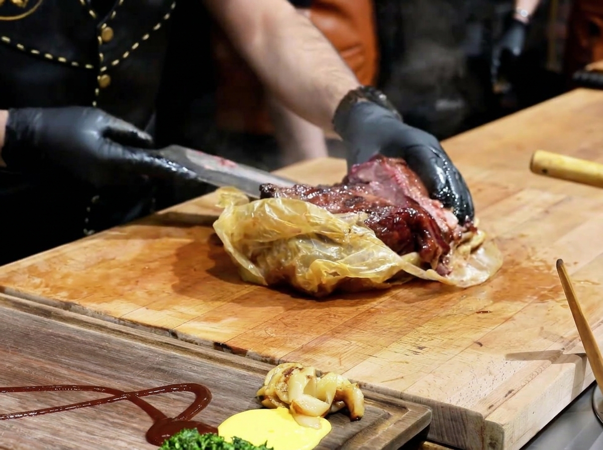 A chef using a knife to open a translucent cooking wrap, revealing a dark, succulent cooked brisket on a wooden board.