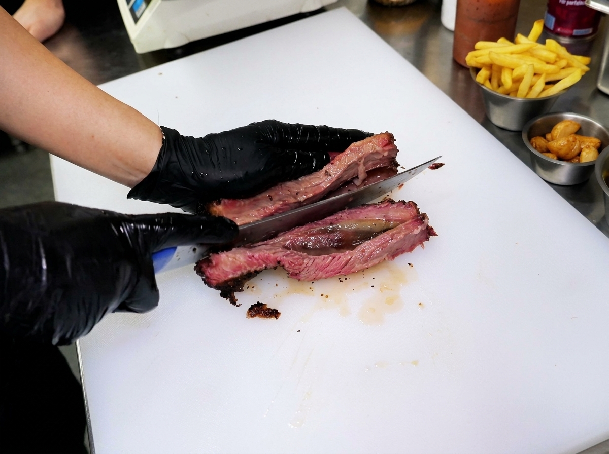 Slicing through a thick piece of tender smoked beef rib on a white cutting board, showing the perfect pink interior.