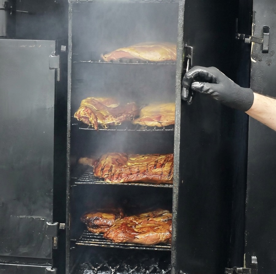 Partially smoked, browned cuts of beef resting on the grates of a large, open smoker.