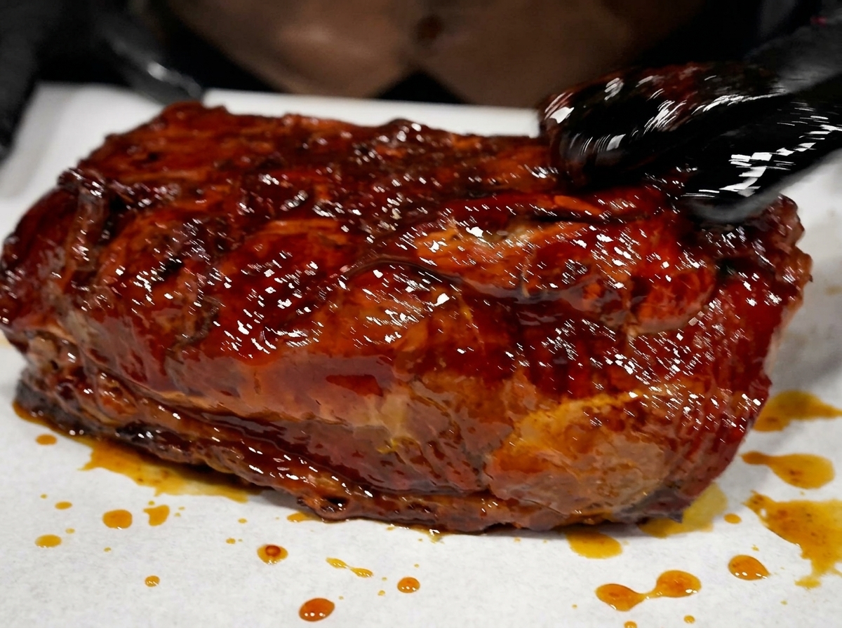 A piece of smoked beef glistening with dark marinade resting on a sheet before being wrapped.