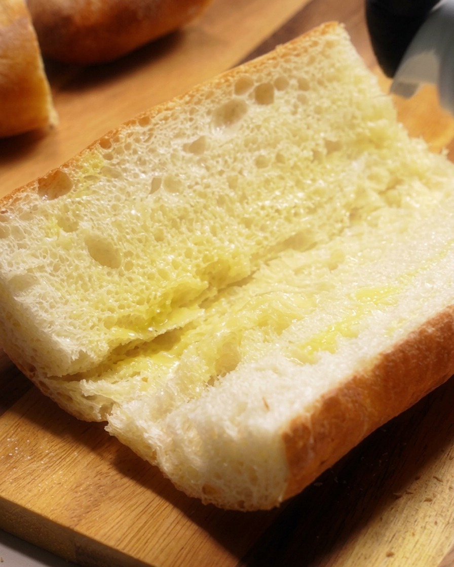 Close-up of a crusty baguette sliced horizontally with melted butter brushed generously across the porous inside crumb.