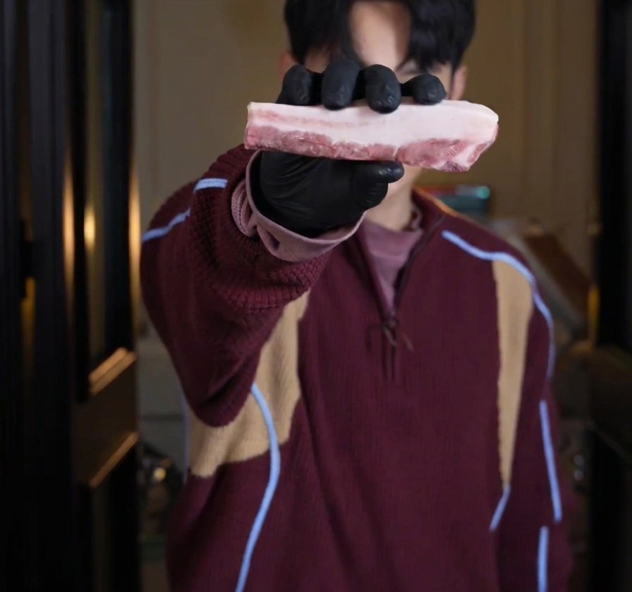 A person wearing black gloves holding up a thick, raw slab of layered pork belly.