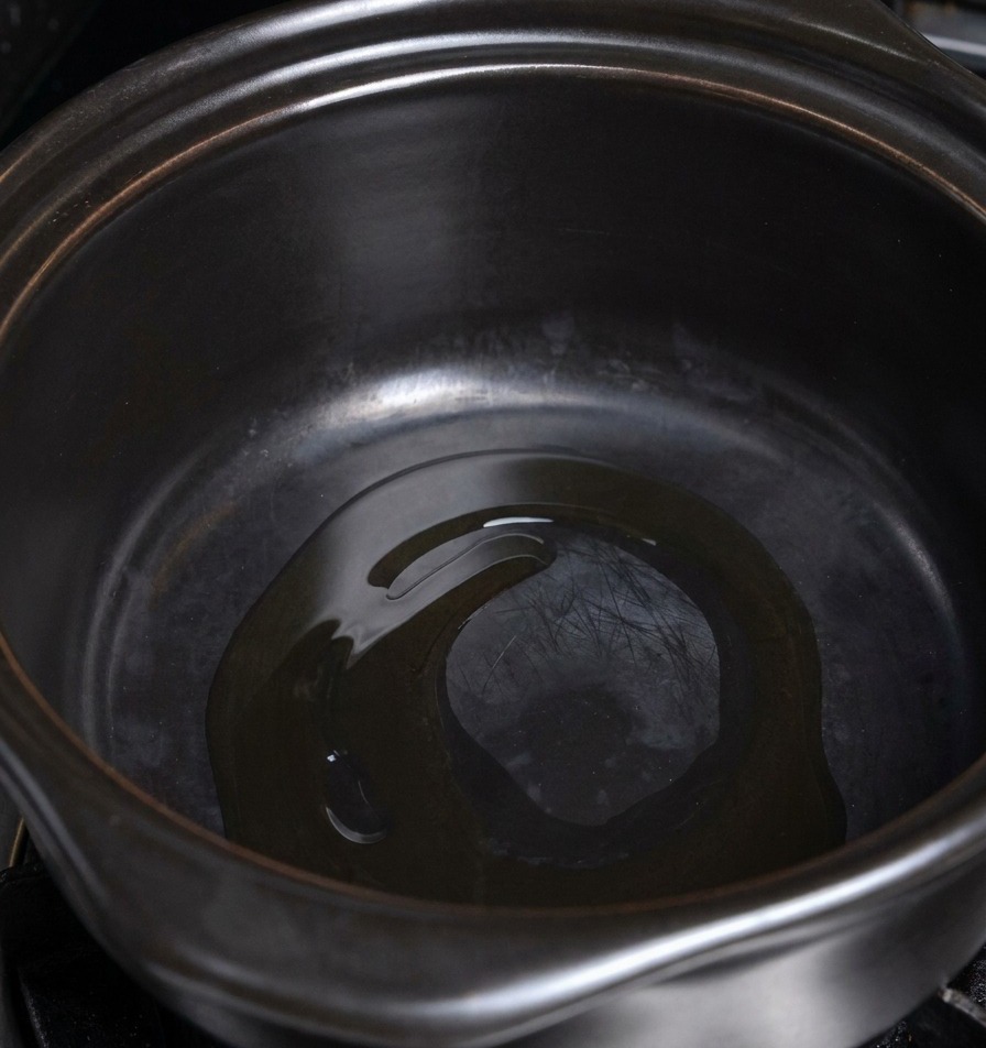 A thin layer of cooking oil shimmering at the bottom of a heated dark ceramic pot.