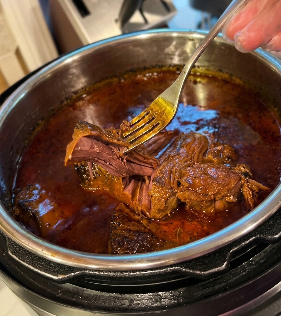 A metal fork effortlessly pulling apart extremely tender, slow-cooked beef sitting in a rich, dark sauce inside a pot.