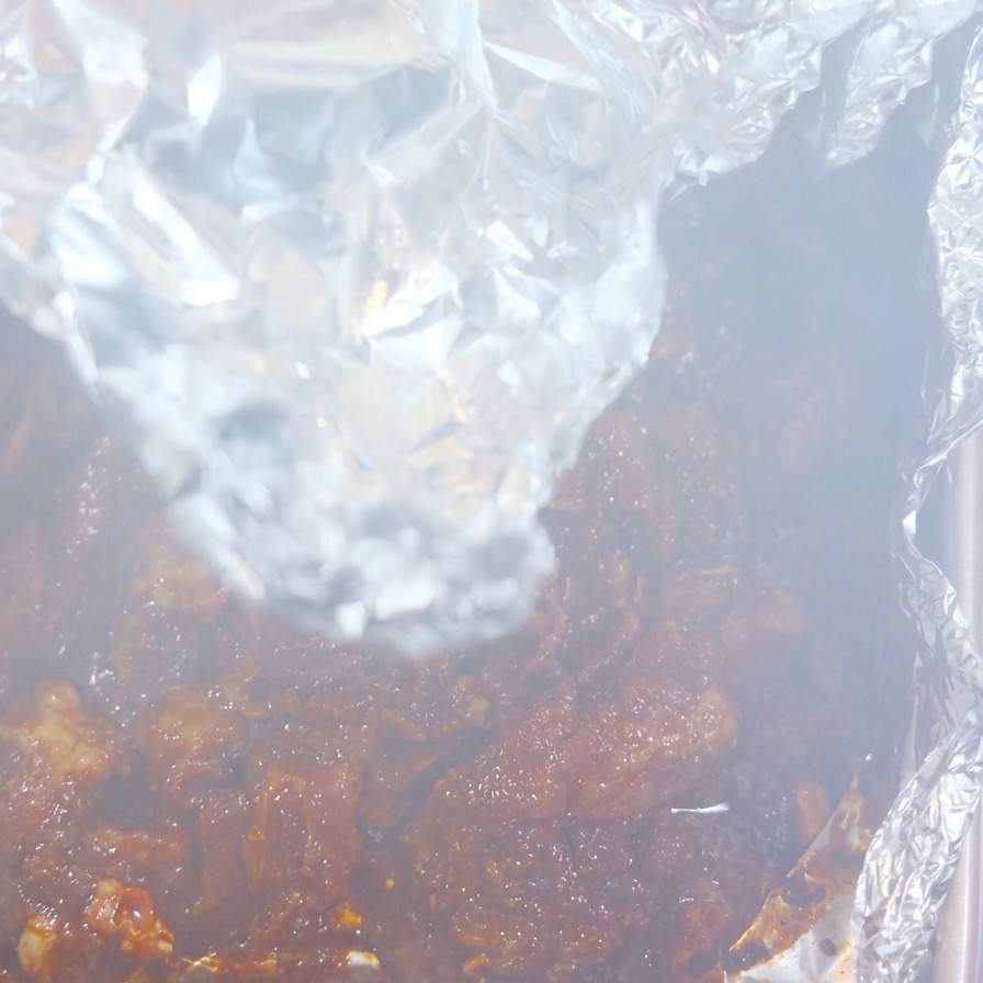 Steam rising from a freshly opened aluminum foil packet, revealing dark, succulent, and heavily spiced cooked pork.