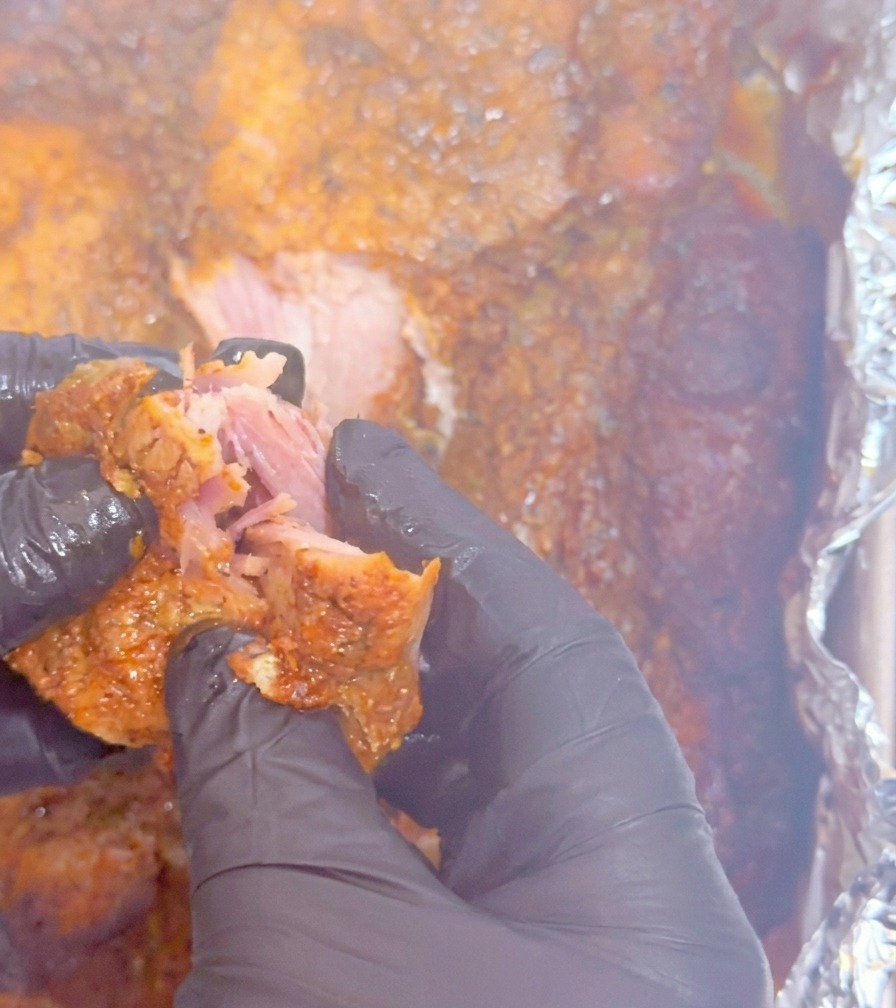 Hands in black gloves pulling apart a tender piece of slow-cooked pork, showing the succulent, shredded texture.