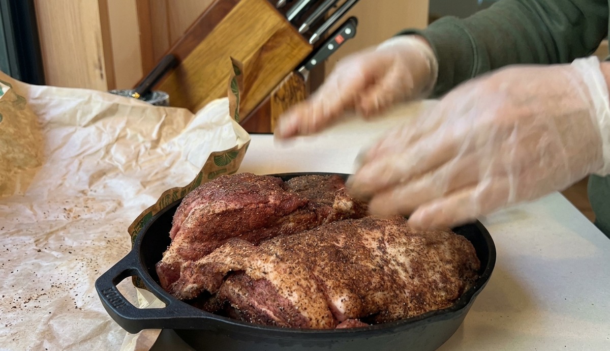 A seasoned pork shoulder sitting in a cast iron skillet, ready to be slow-baked in a preheated oven.