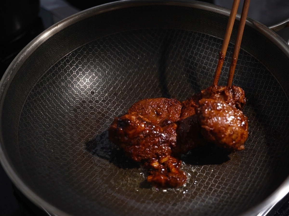 Marinated pork chunks being seared with chopsticks in a hot wok, showing a nicely browned crust.