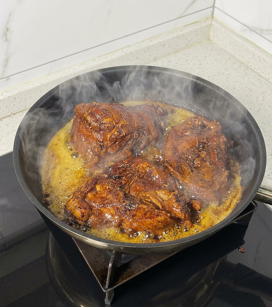 Three large pieces of seasoned pork browning and sizzling in a black skillet with visible steam and bubbling oil.