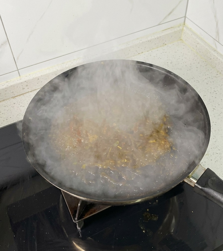 A frying pan on a stovetop filled with boiling, reducing braising liquid, releasing a thick cloud of steam.