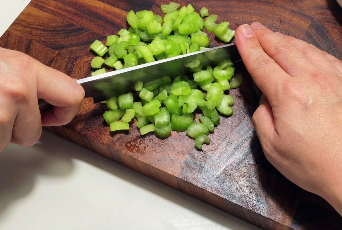A white onion being finely diced into small pieces on a wooden cutting board.