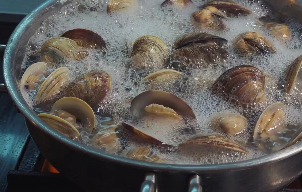 Fresh clams bubbling in a pan of boiling water, with most shells fully open to reveal the meat.
