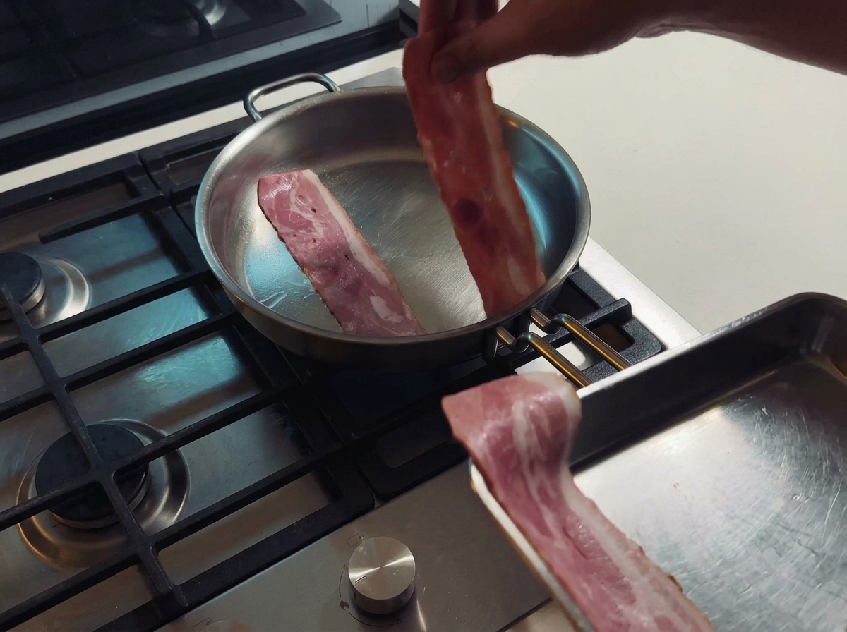 Two strips of bacon frying in a stainless steel pan as they release their natural fat.