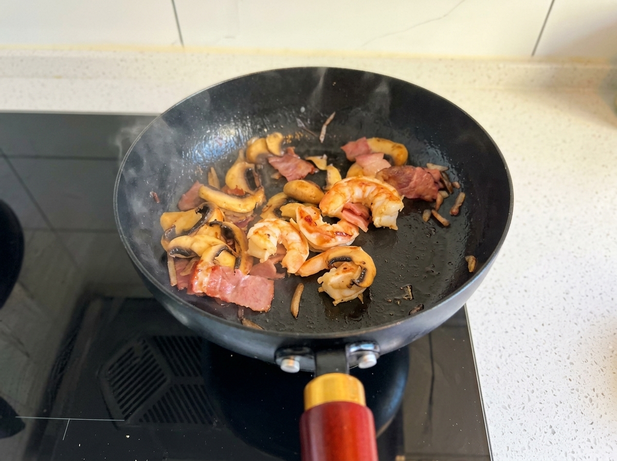 Sautéing shrimp, bacon, and mushrooms in a black pan until the shrimp turn pink and opaque.