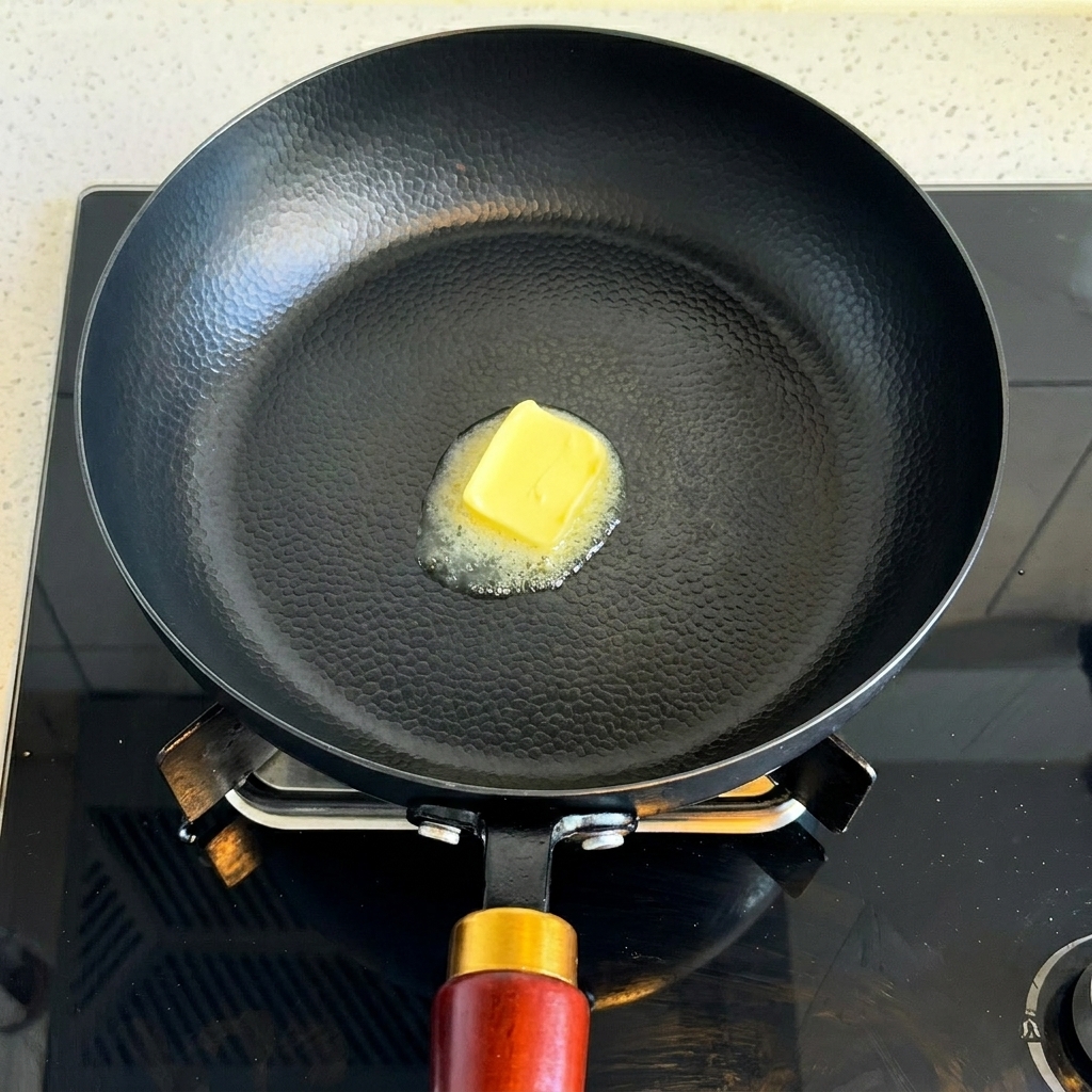 A square piece of yellow butter melting in a hot black frying pan.