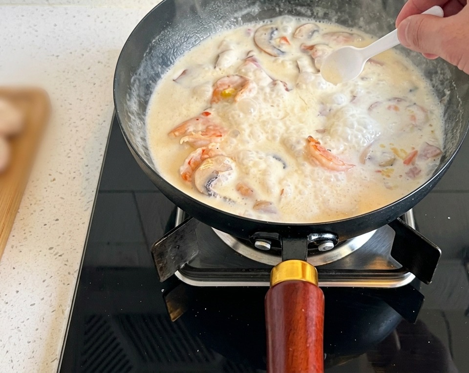 A small white spoon adding a pinch of salt to a bubbling pan of cream of mushroom soup.