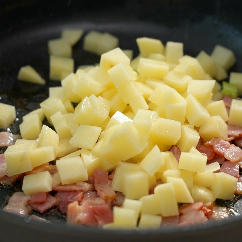 Diced potatoes being dropped into a frying pan over chopped bacon.