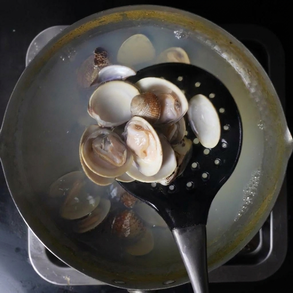 A black slotted spoon scooping opened clams out of a pot of boiling water.