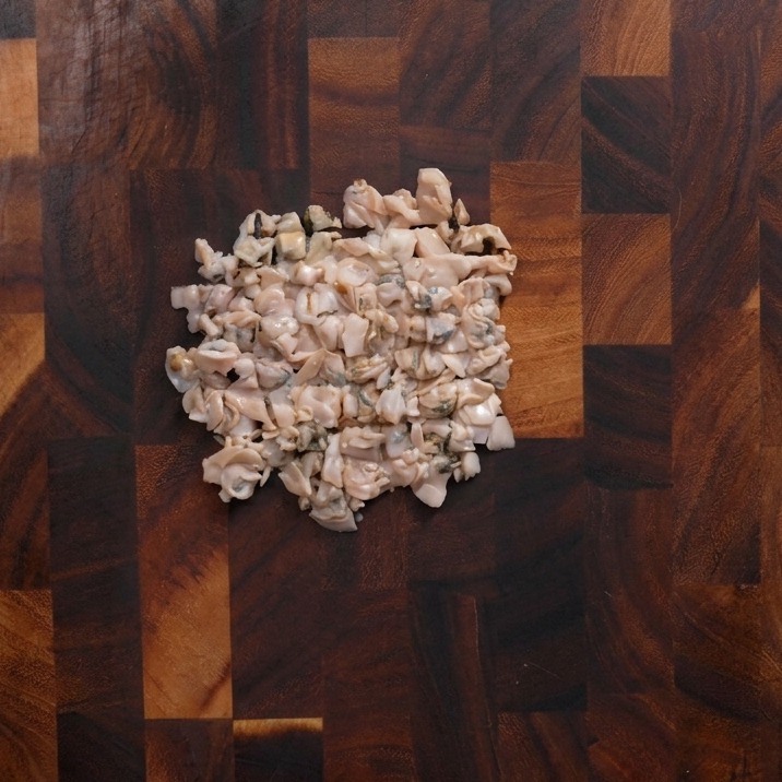 A pile of roughly chopped clam meat resting in the center of a dark wooden cutting board.