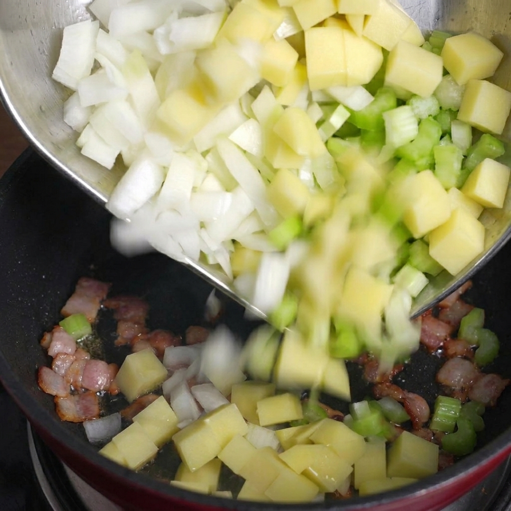 Pouring diced potatoes, celery, and onions from a metal bowl into a pan with cooked bacon pieces.