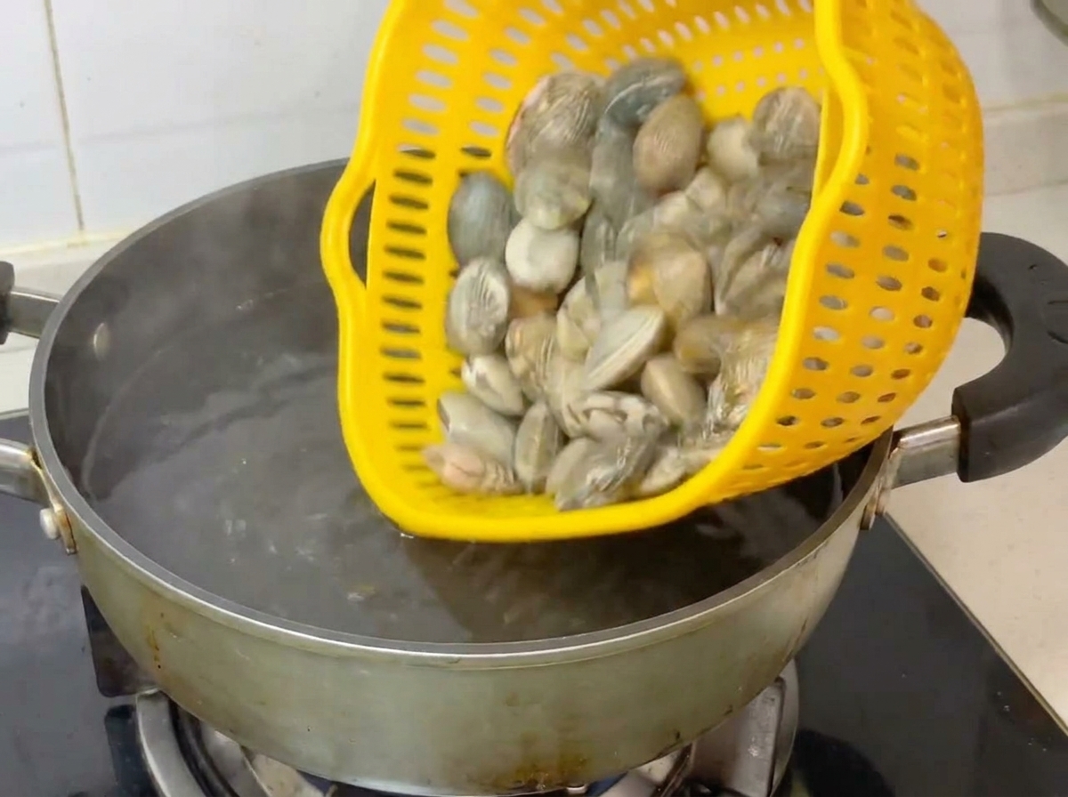 Whole clams being poured from a yellow colander into a pot of boiling water.
