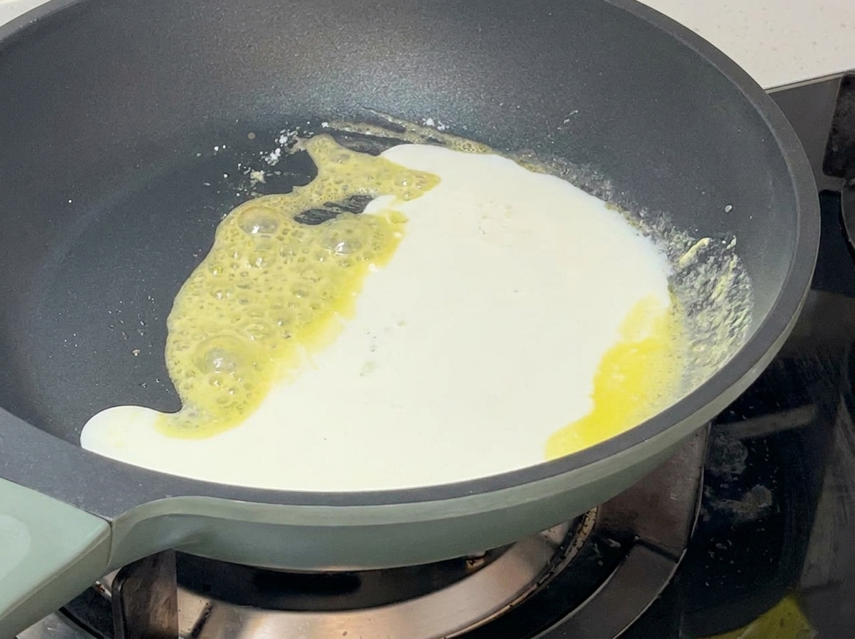 White milk and cream mixture being poured into a pan with yellow bubbling roux, creating a thick white sauce.