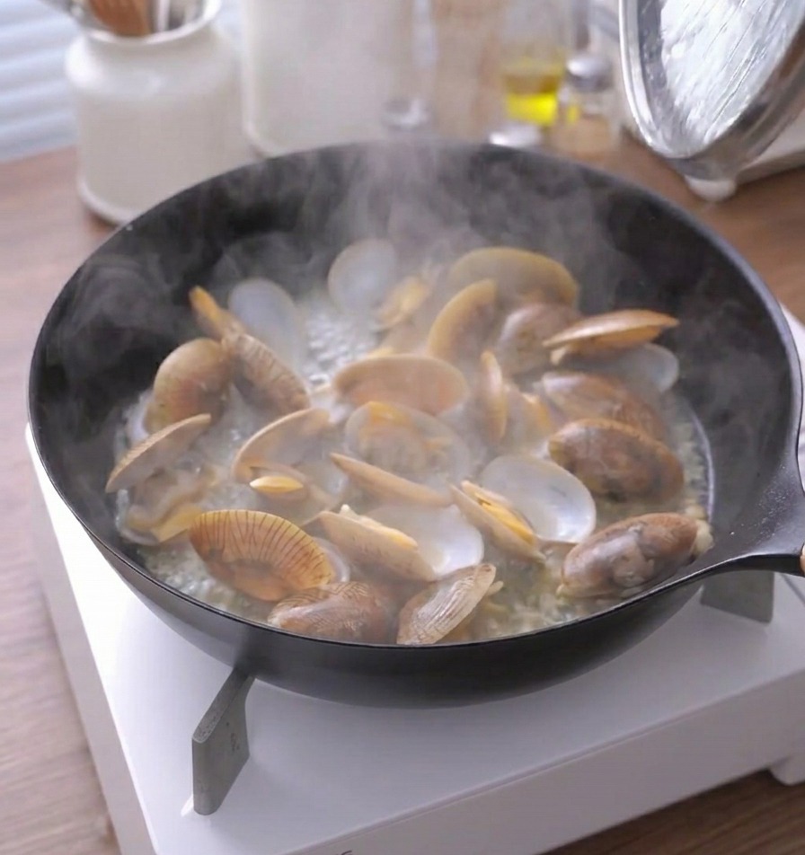 Steam rising heavily from a pan of cooked clams with their shells open.