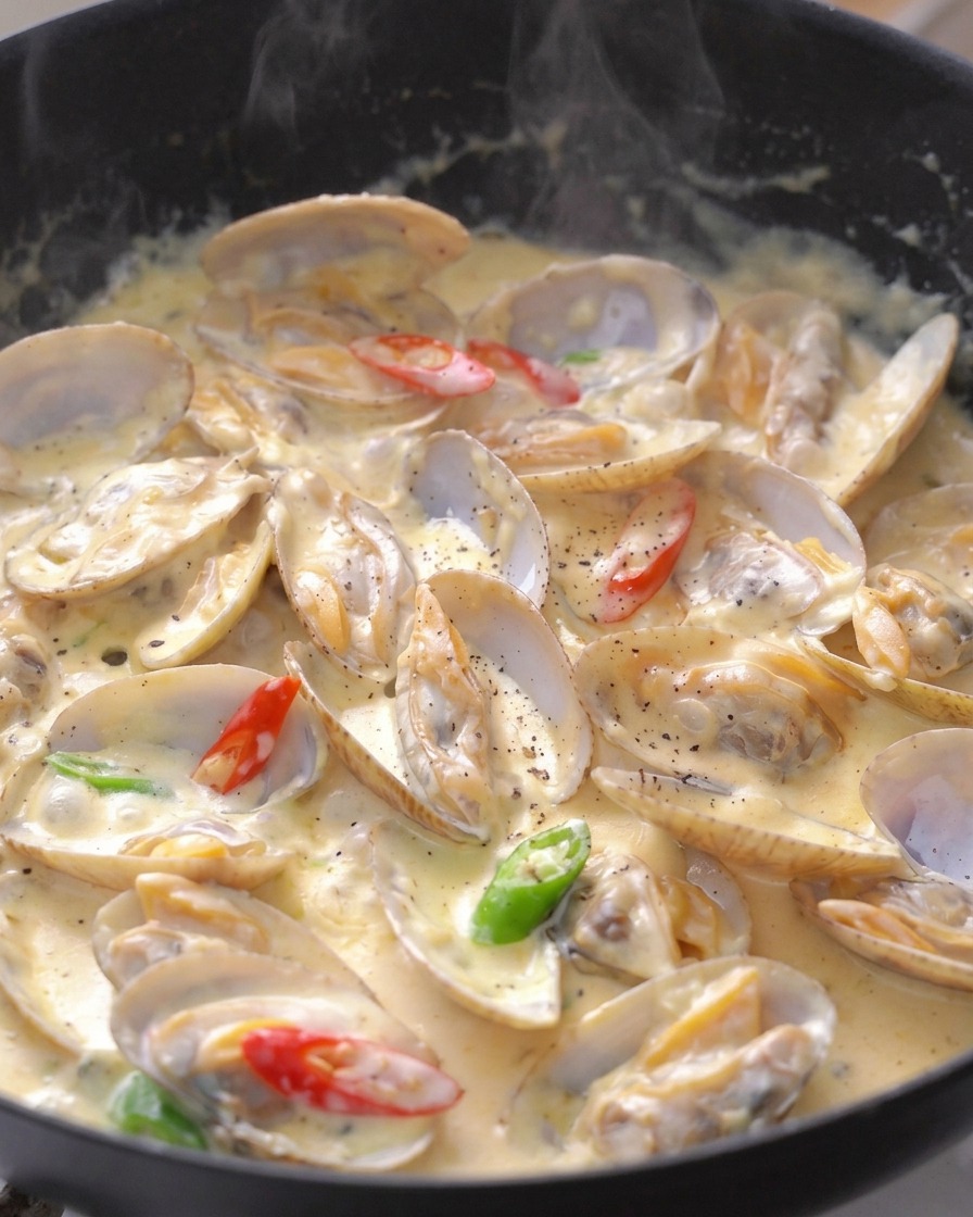 Creamy cooked clams in a pan, garnished with sliced red and green chili peppers and cracked black pepper.