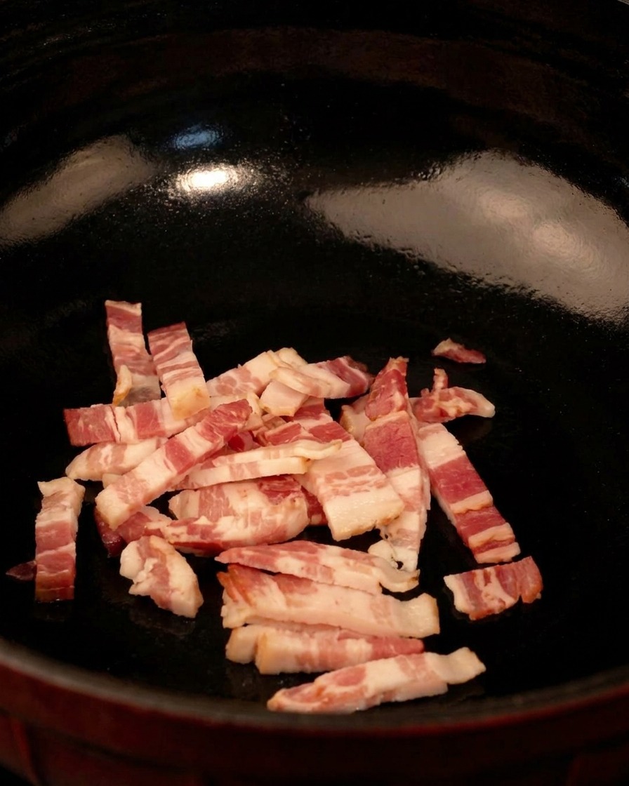 Raw diced bacon strips in a black skillet, ready to be cooked over medium heat.