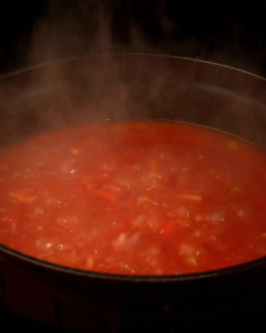 A steaming, bubbling pot of red tomato-based clam chowder simmering on the stove.