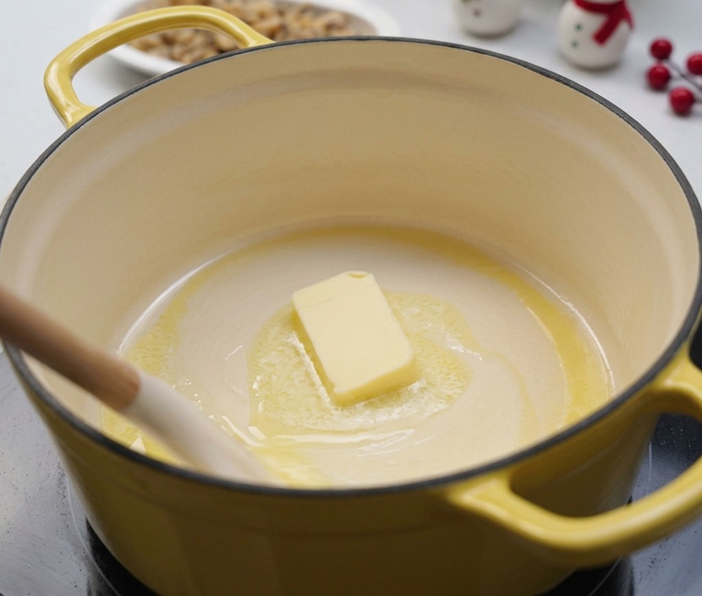 A block of butter melting in a yellow pot over low heat, gently stirred by a white spatula.