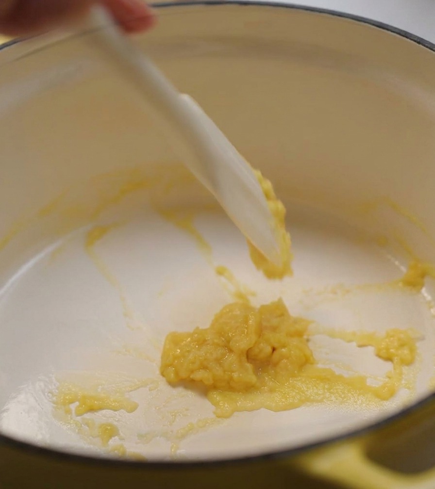 A white silicone spatula stirring a thick, pale yellow butter and flour paste in a yellow pot.