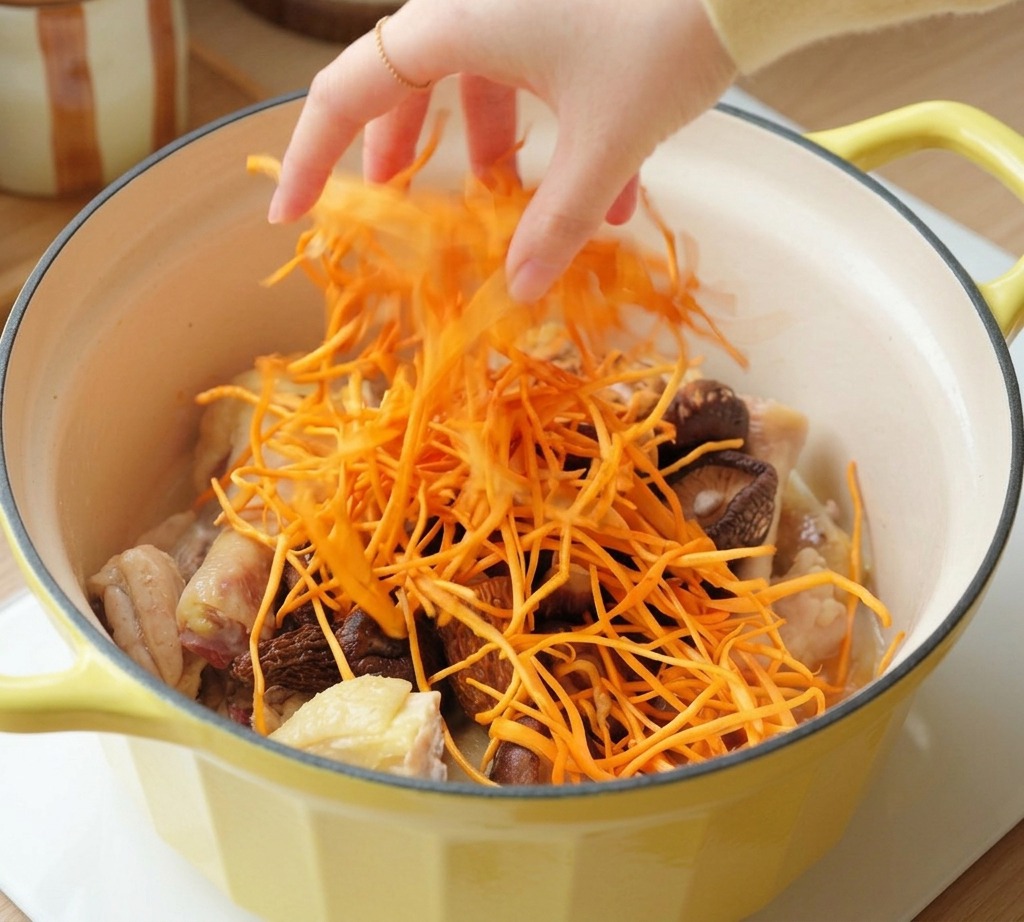 A hand sprinkling bright orange cordyceps flowers over chicken and mushrooms in a yellow pot.