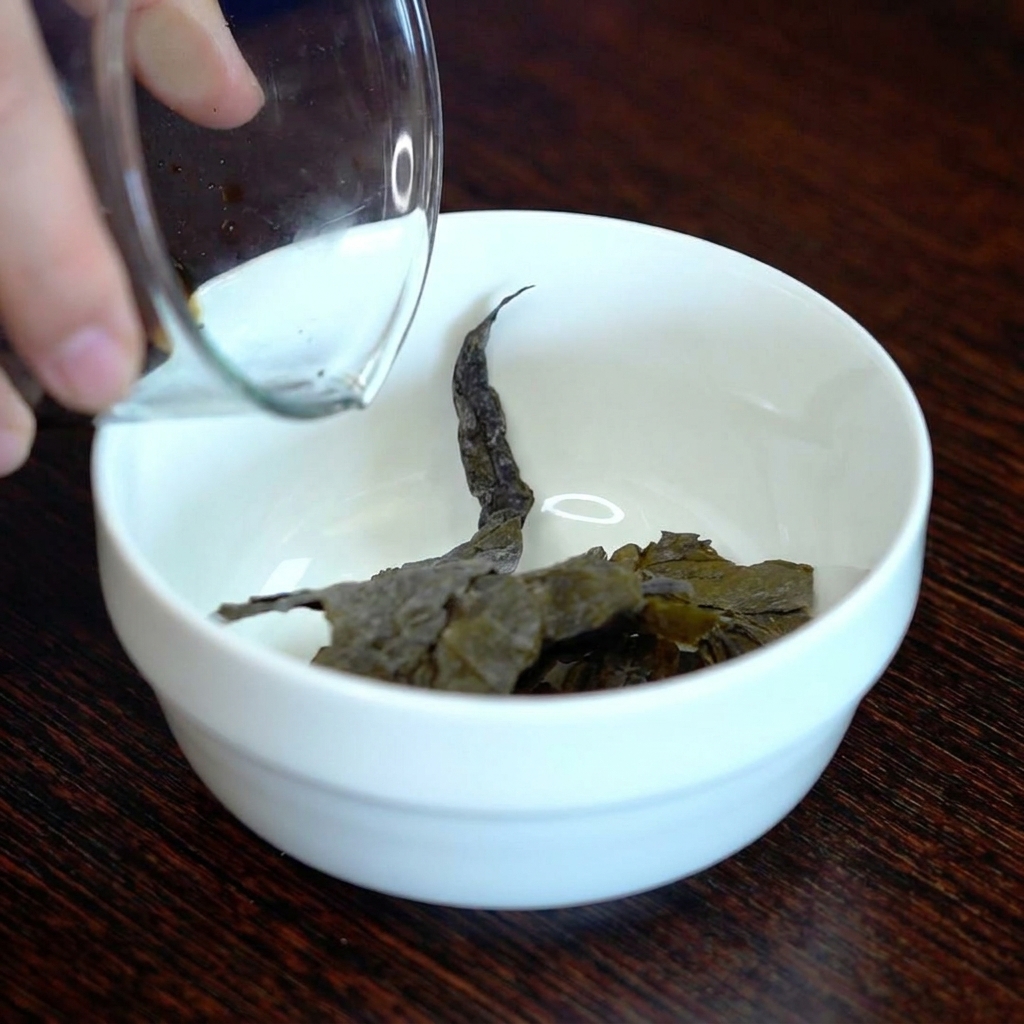 Dark soy sauce being poured over a piece of dried kombu in a small white ceramic bowl.