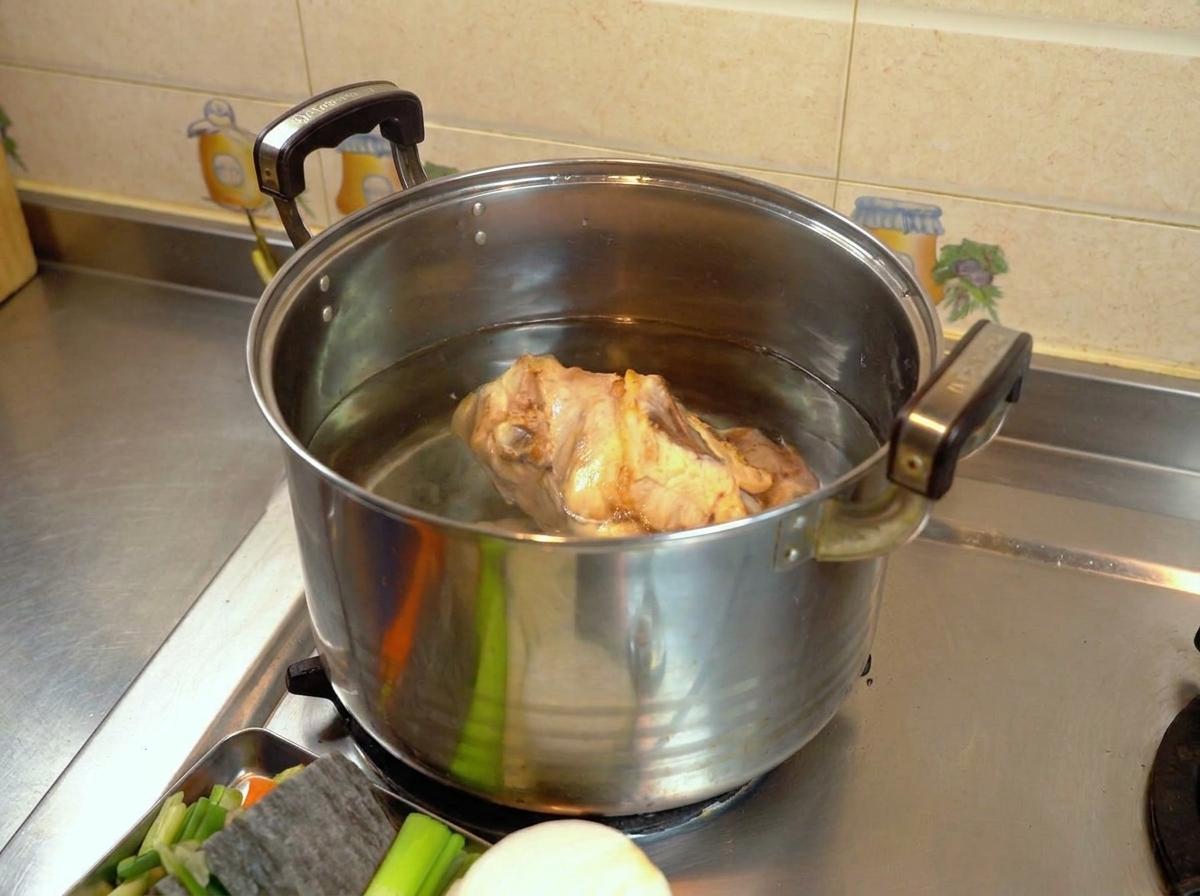 A blanched chicken carcass sitting in a large metal pot filled with clear water on a stovetop.