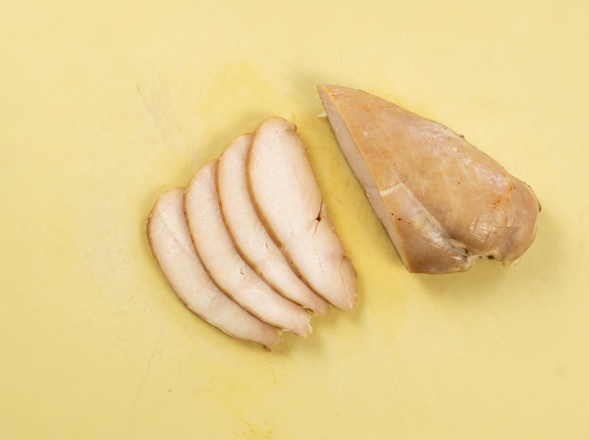 Thin, even slices of lightly browned cooked chicken breast arranged on a yellow cutting board.