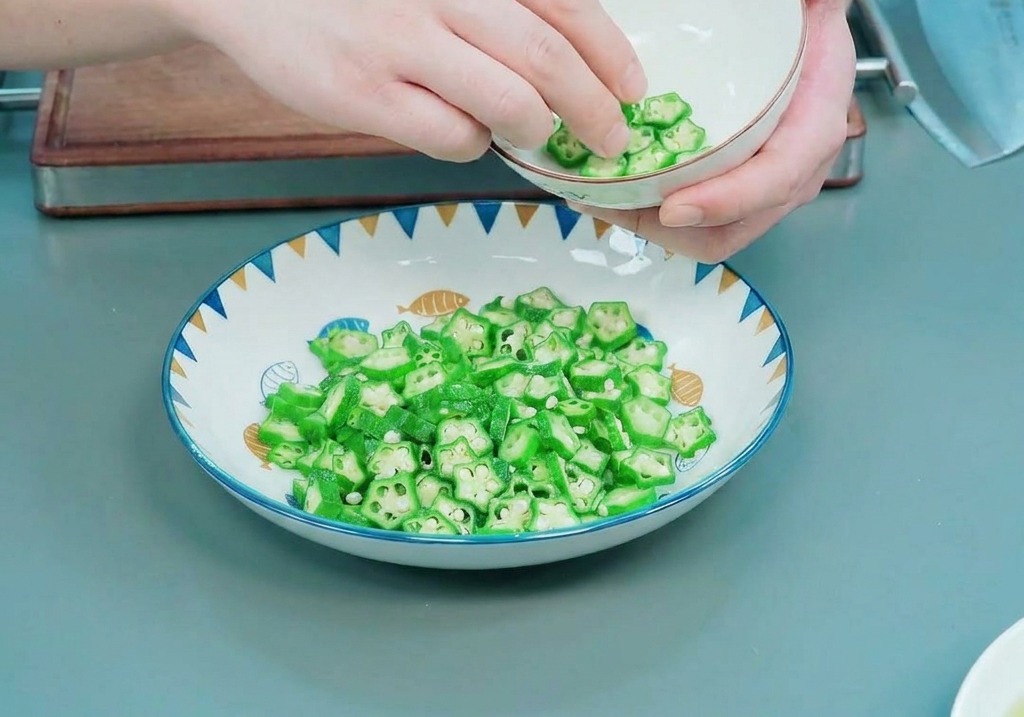 Hands carefully lining the inside of a small white bowl with bright green, star-shaped okra slices.